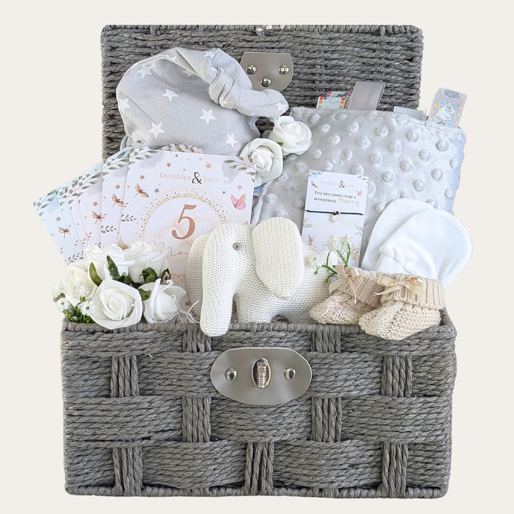 Large baby shower hamper basket with neutral white gifts including elephant baby rattle, taggie blanket, baby hat, mittens and booties.