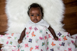 Large cotton muslin swaddle blanket with butterfly print in pinks and purples Shown with baby. 