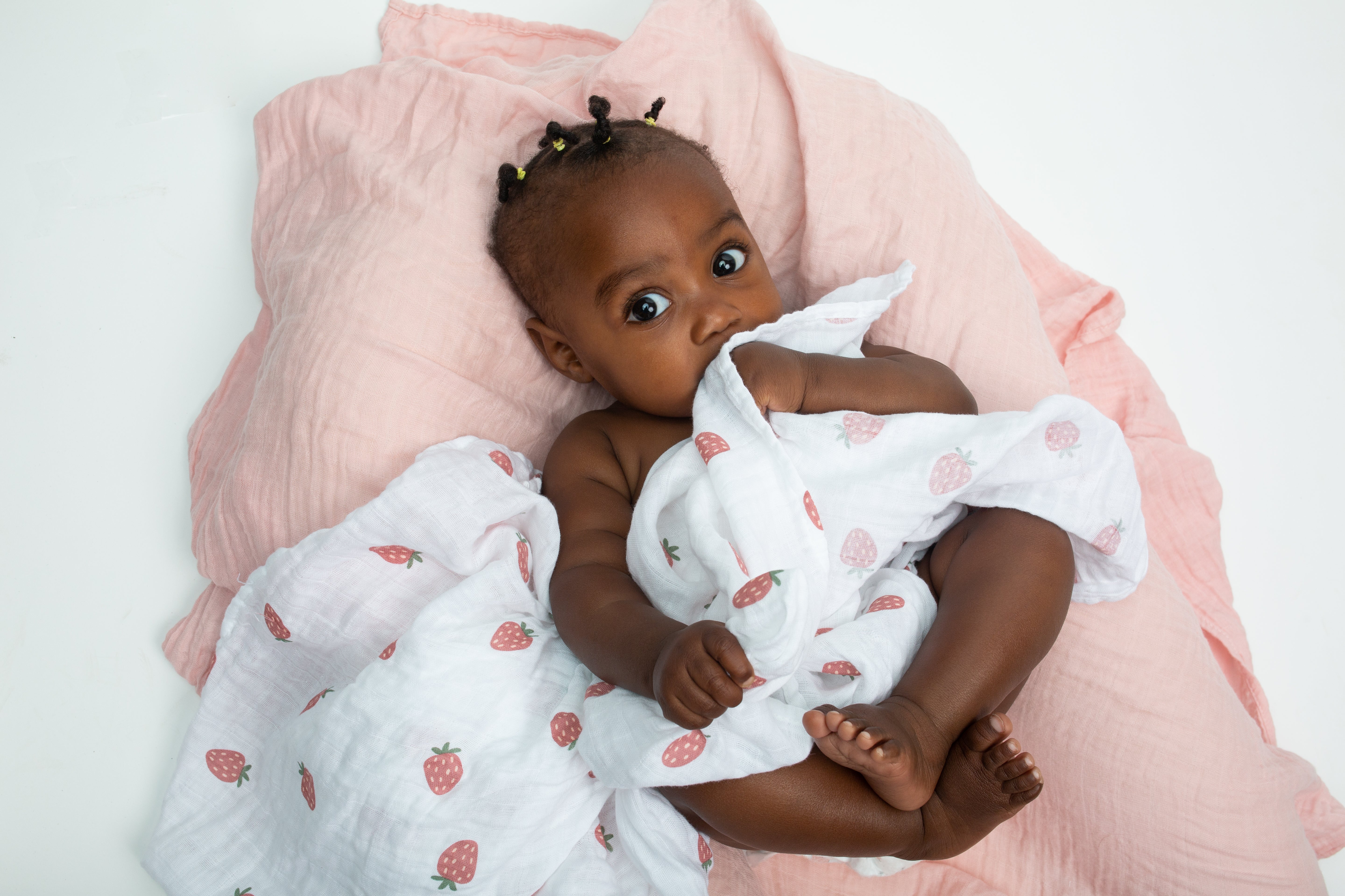 large cotton strawberry print muslin swaddle blanket shown with baby.  Measuring 100 x 100cm, can be used as a swaddling blankets and for nursing.