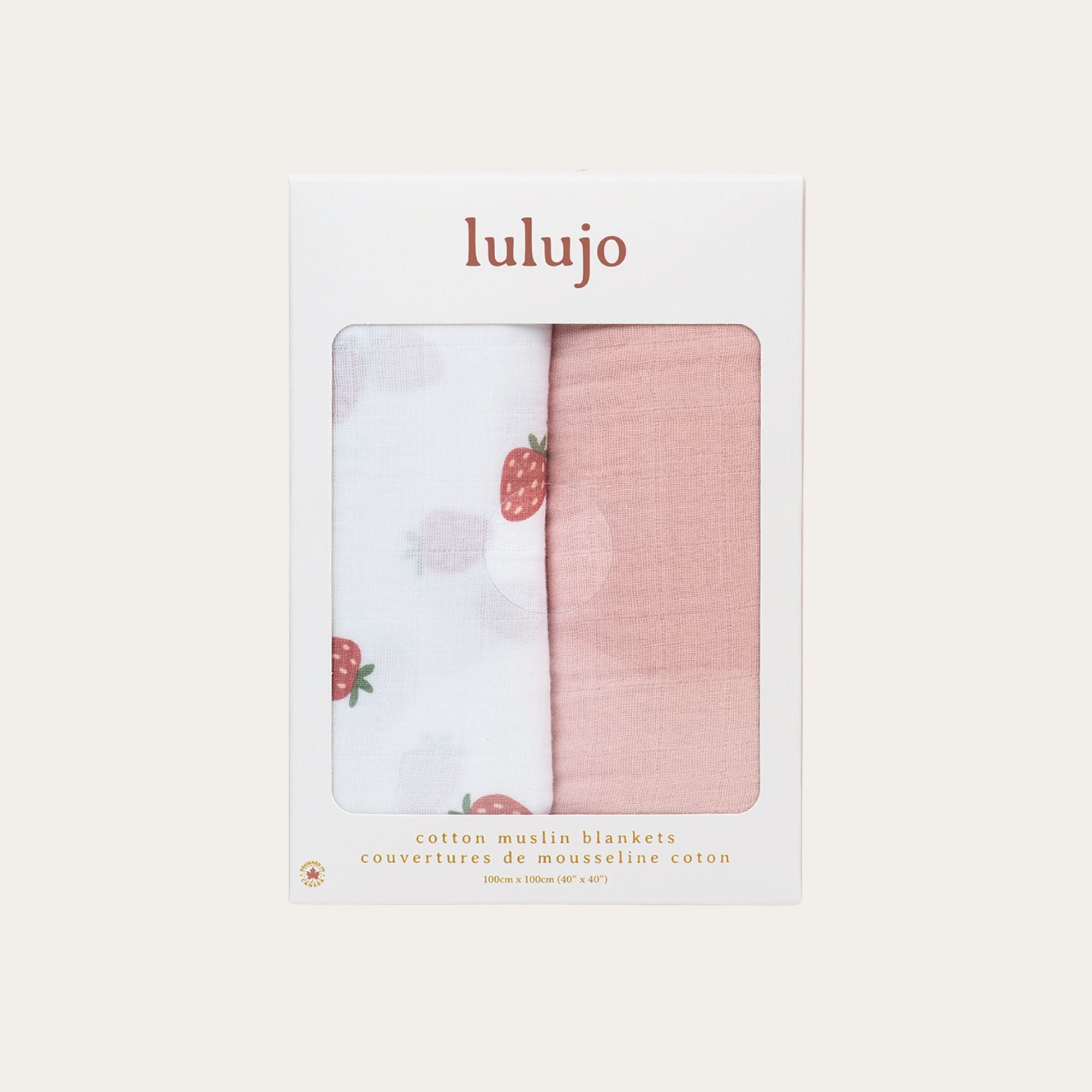 Two-pack of large cotton muslin swaddle blankets displayed in a box. One features a white strawberry print, and the other is a solid dusky pink. 