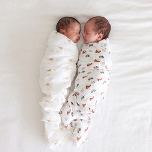 Two cotton muslin baby swaddles with barnyard and chick designs, folded neatly on a surface.