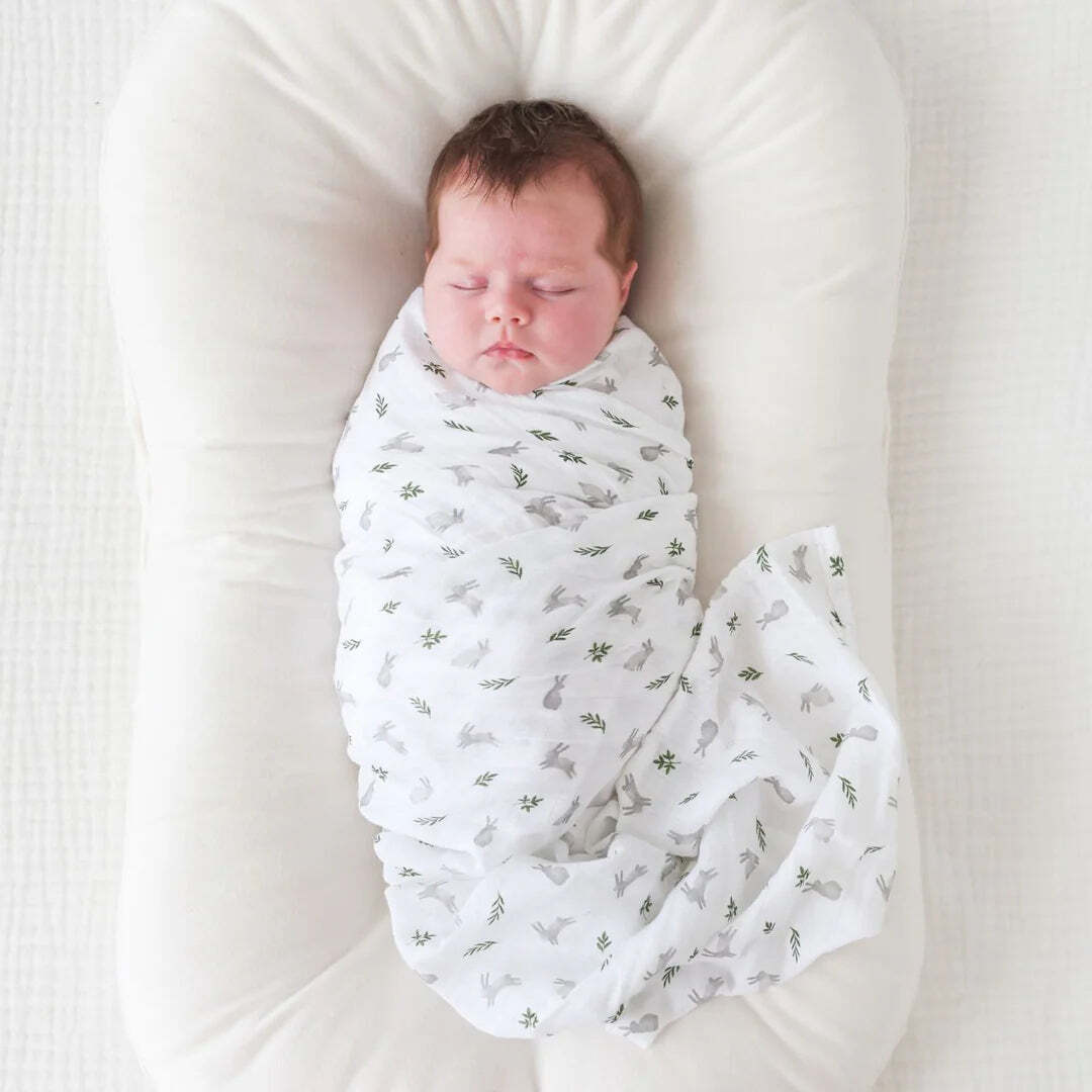 Two cotton muslin baby swaddles with bunny and fern designs, folded neatly on a surface.