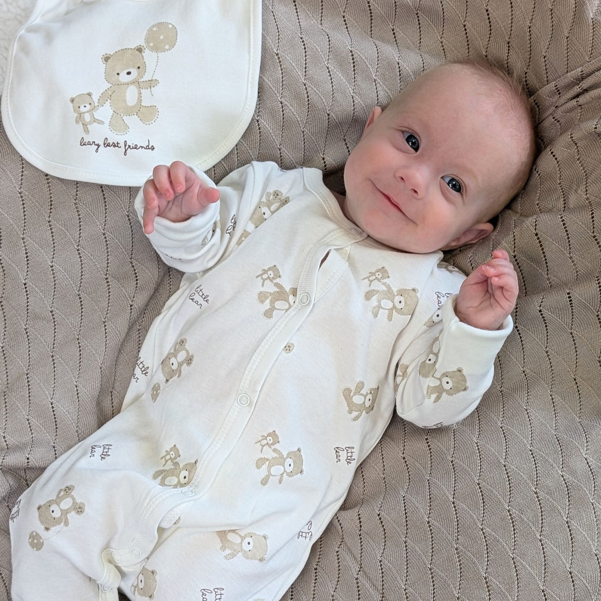 Baby wearing a cream clothing set with bears and balloons.