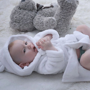 white baby dressing gown worn by baby lying down.