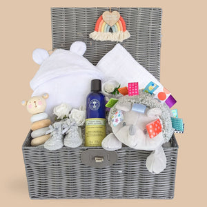 New baby hamper basket with gifts including white baby bath robe, soft taggie hedgehog and skincare.