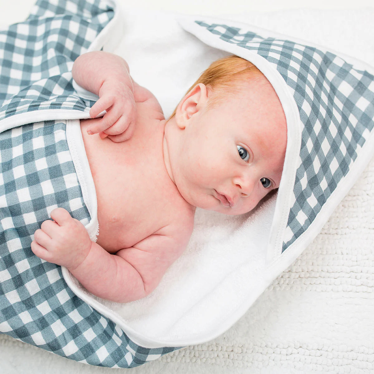 A white and blue gingham hooded towel made with printed muslin and terry cloth, folded and ready for use.