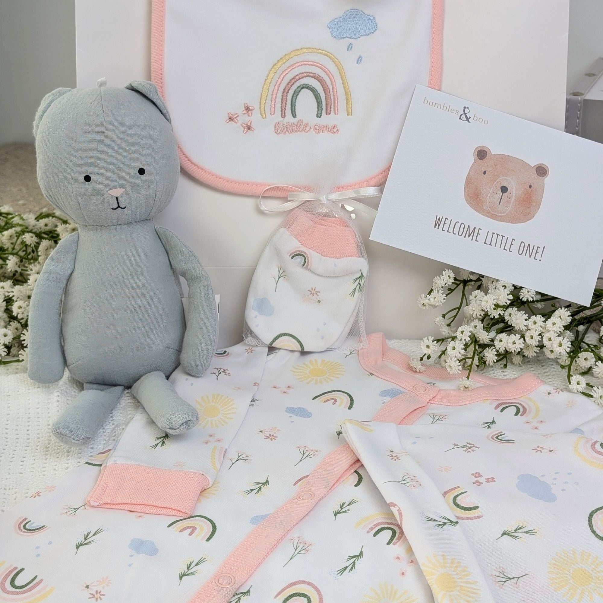 New baby girl clothing gifts hamper with a five piece rainbow themed clothing set and grey organic kitten soft toy. Presented in a hamper bag.