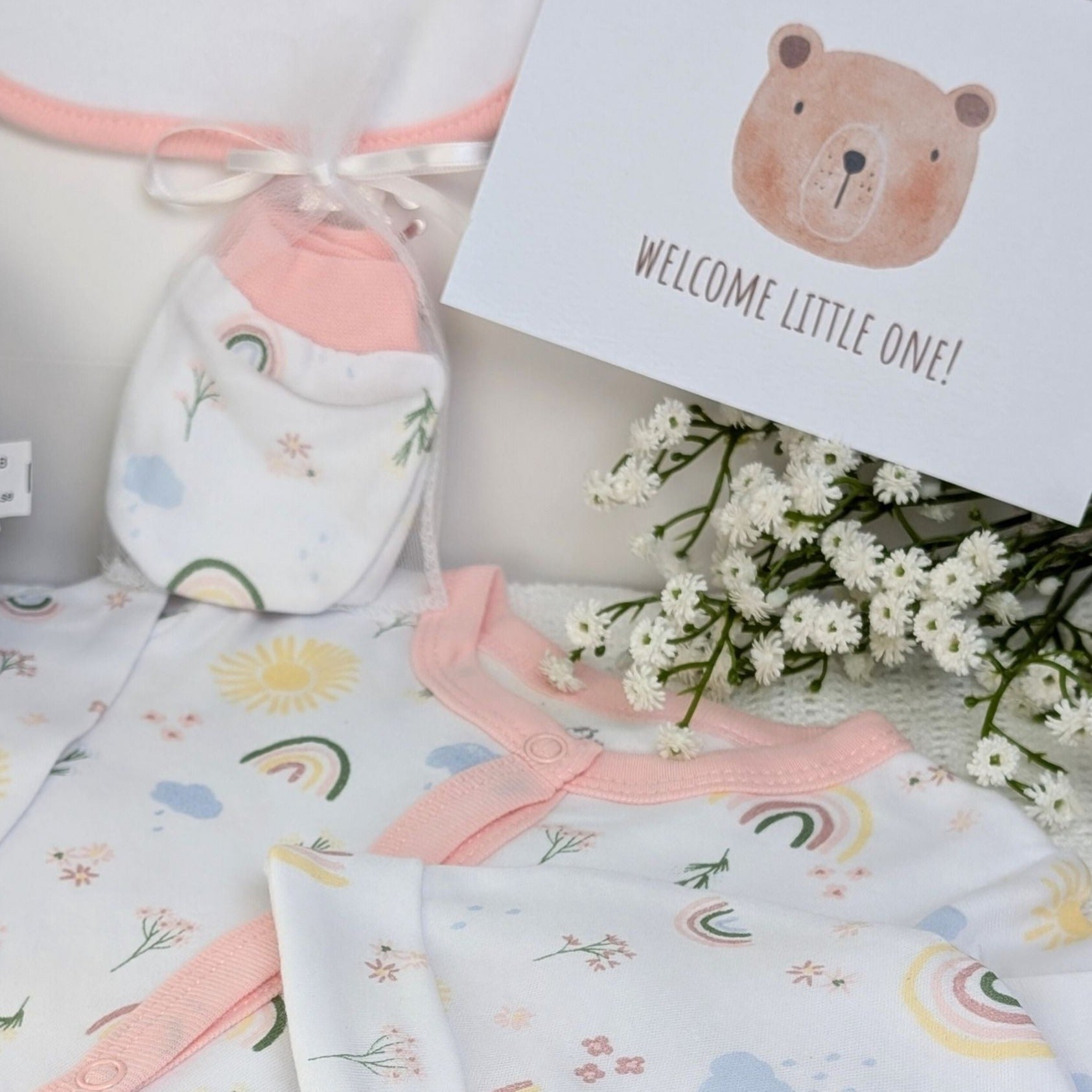 New baby girl clothing gifts hamper with a five piece rainbow themed clothing set and grey organic kitten soft toy. Presented in a hamper bag.