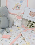 New baby girl clothing gifts hamper with a five piece rainbow themed clothing set and grey organic kitten soft toy. Presented in a hamper bag.