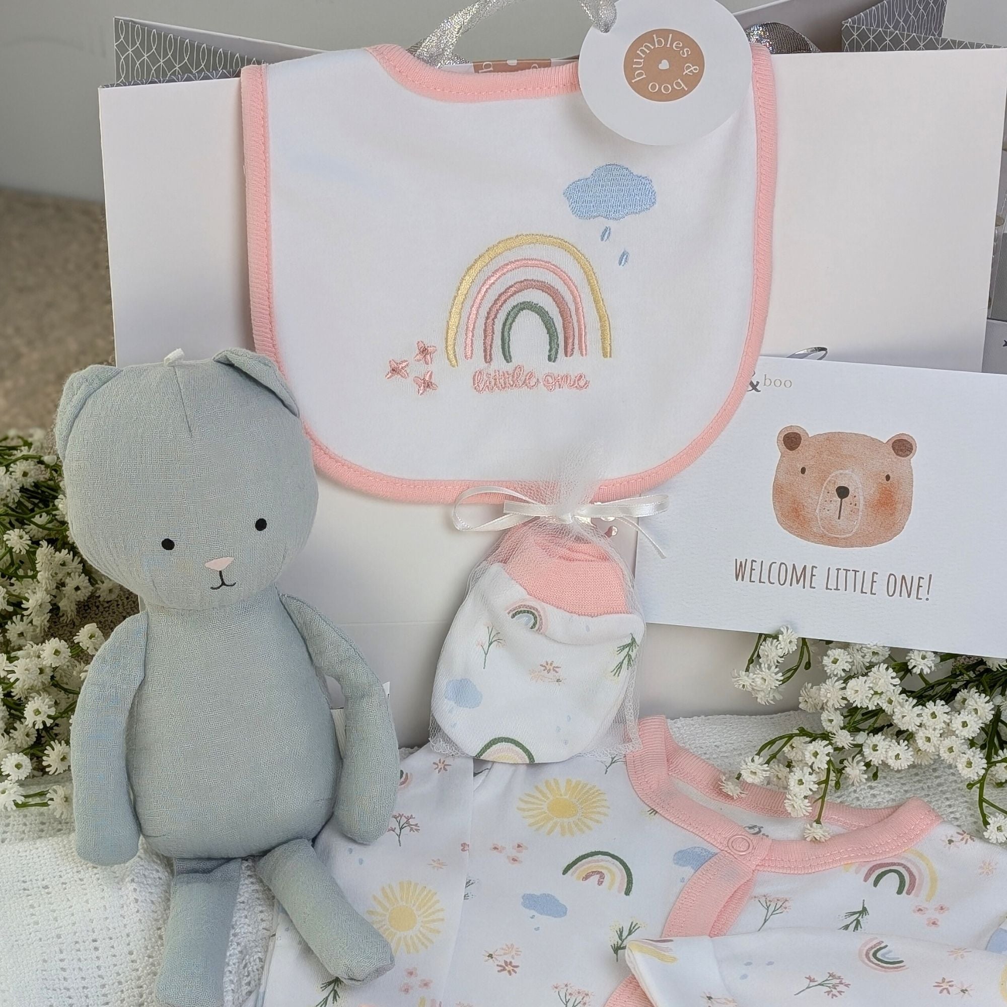 New baby girl clothing gifts hamper with a five piece rainbow themed clothing set and grey organic kitten soft toy. Presented in a hamper bag.