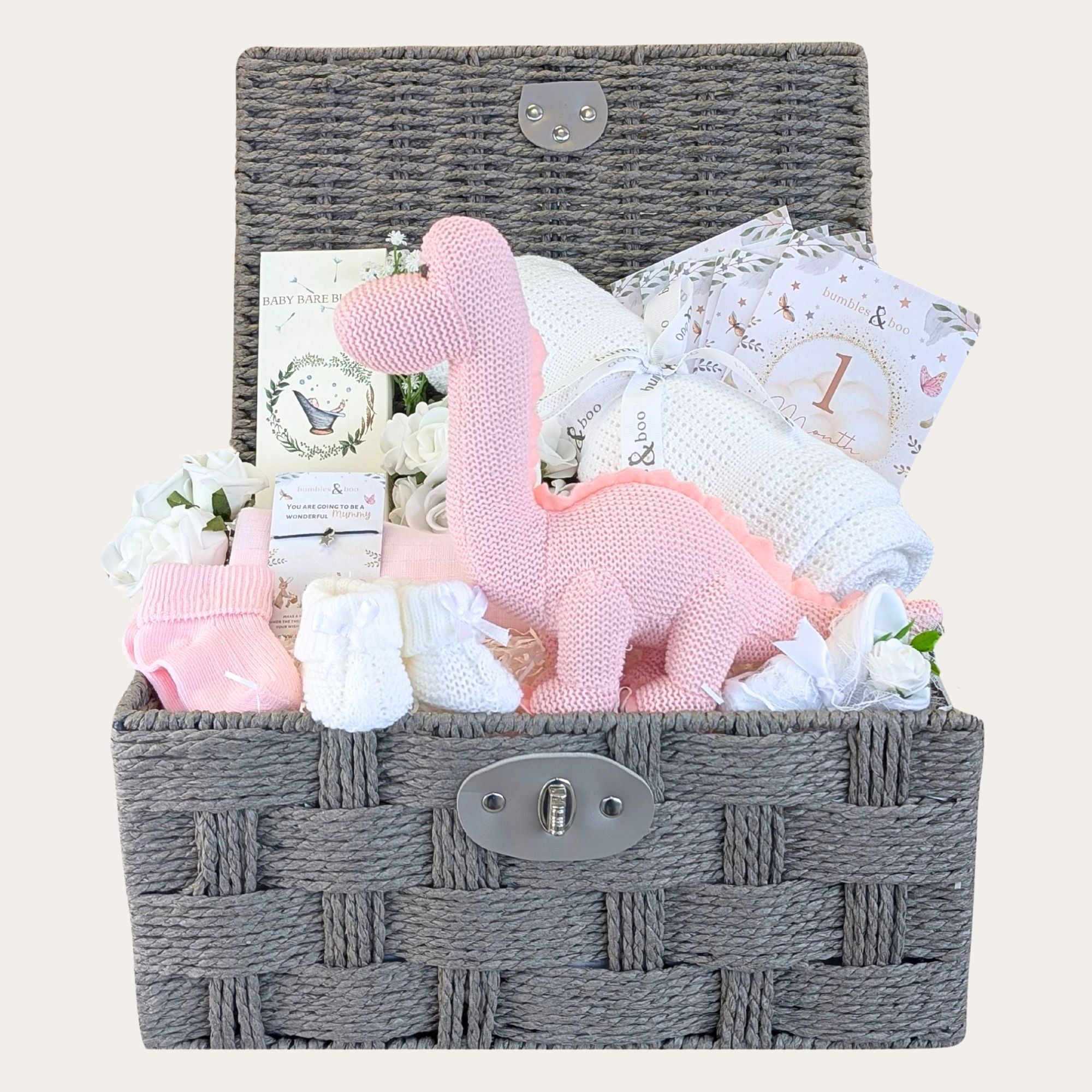 Baby girl gifts including organic pink dinosaur, cellular baby blanket and milestone cards in a dark brown hamper basket.