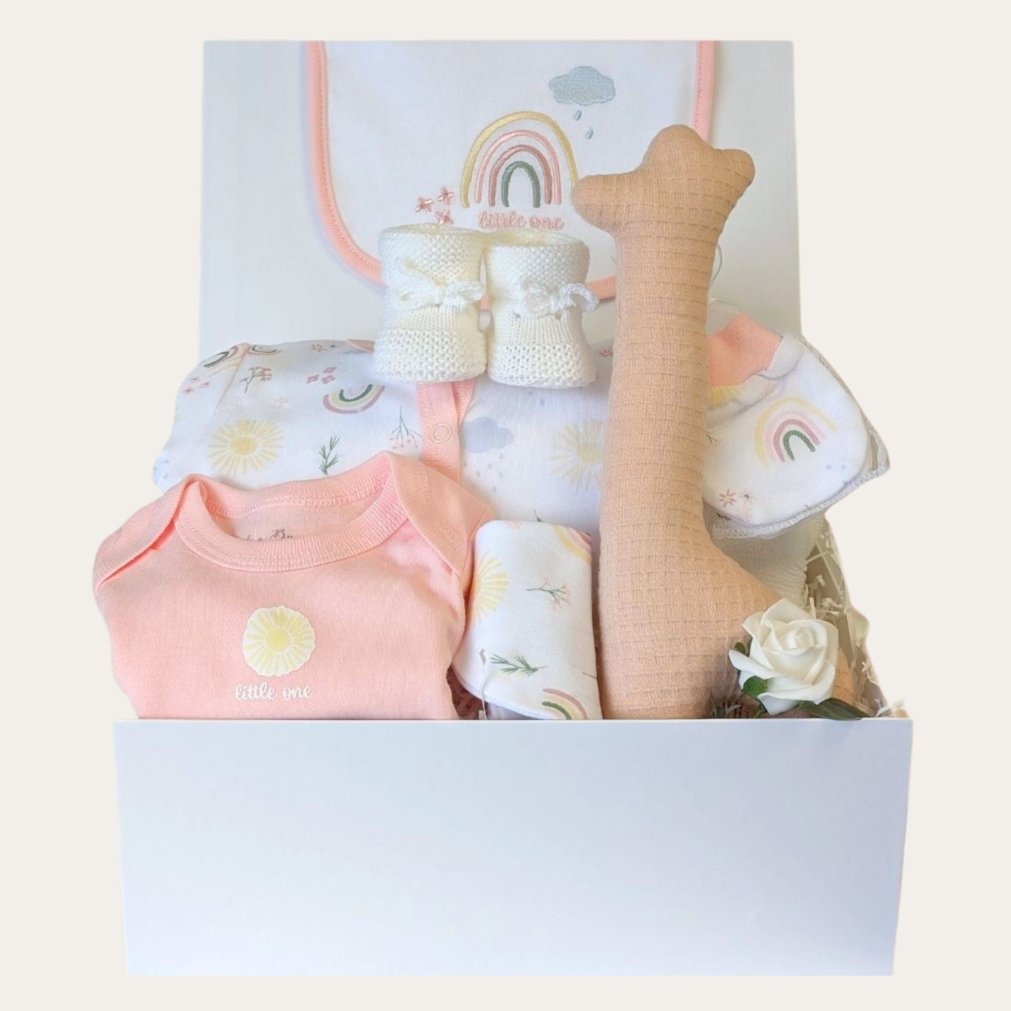 White baby girl gift box with flower and rainbow clothing set packed in a gifts hamper with a giraffe soft toy.