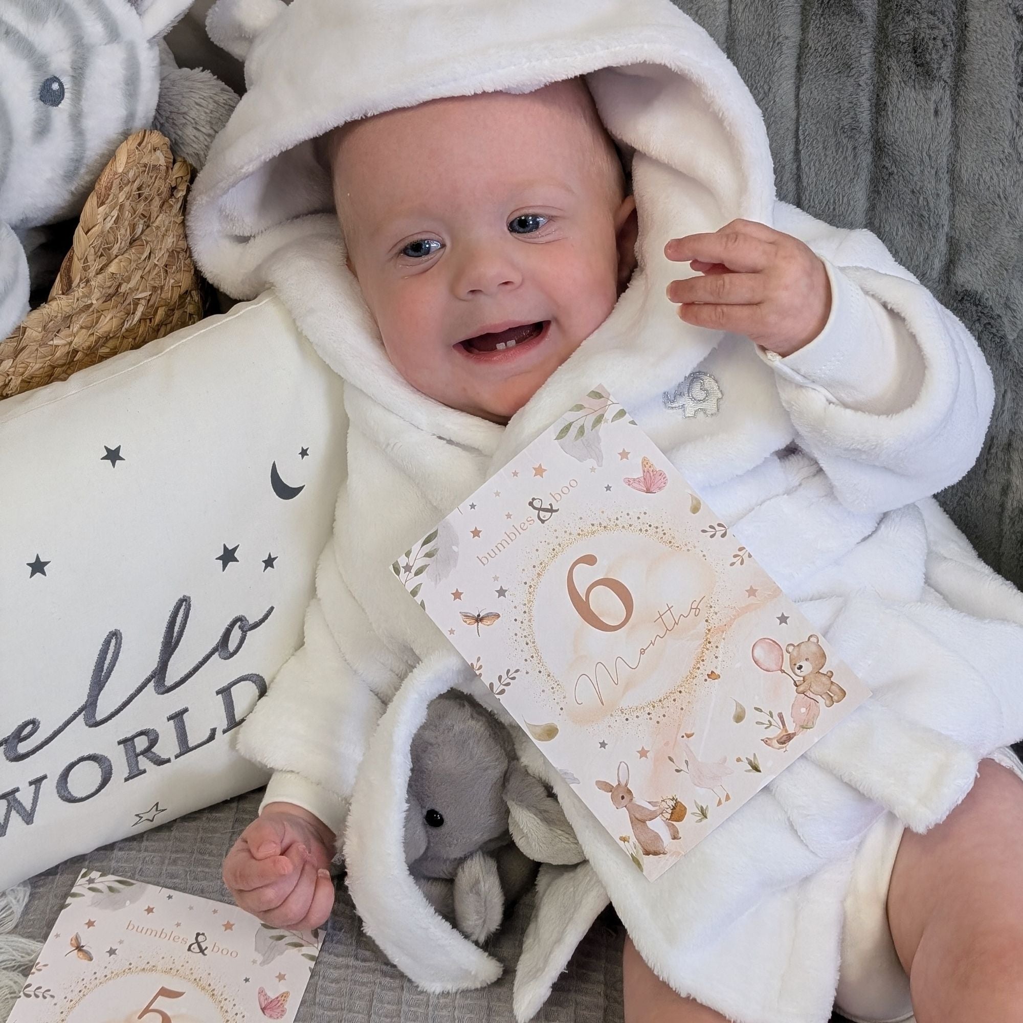 Baby in white dressing gown with a 6 months milestone card.