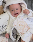 Baby in white dressing gown with a 6 months milestone card.