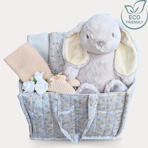 Baby shower gifts hamper in a nappy bag caddy. Presents include baby essentials and grey rabbit plush toy.