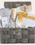 Baby shower hamper gifts basket with muslin soft toy, chocolates and a white cotton cellular blanket.