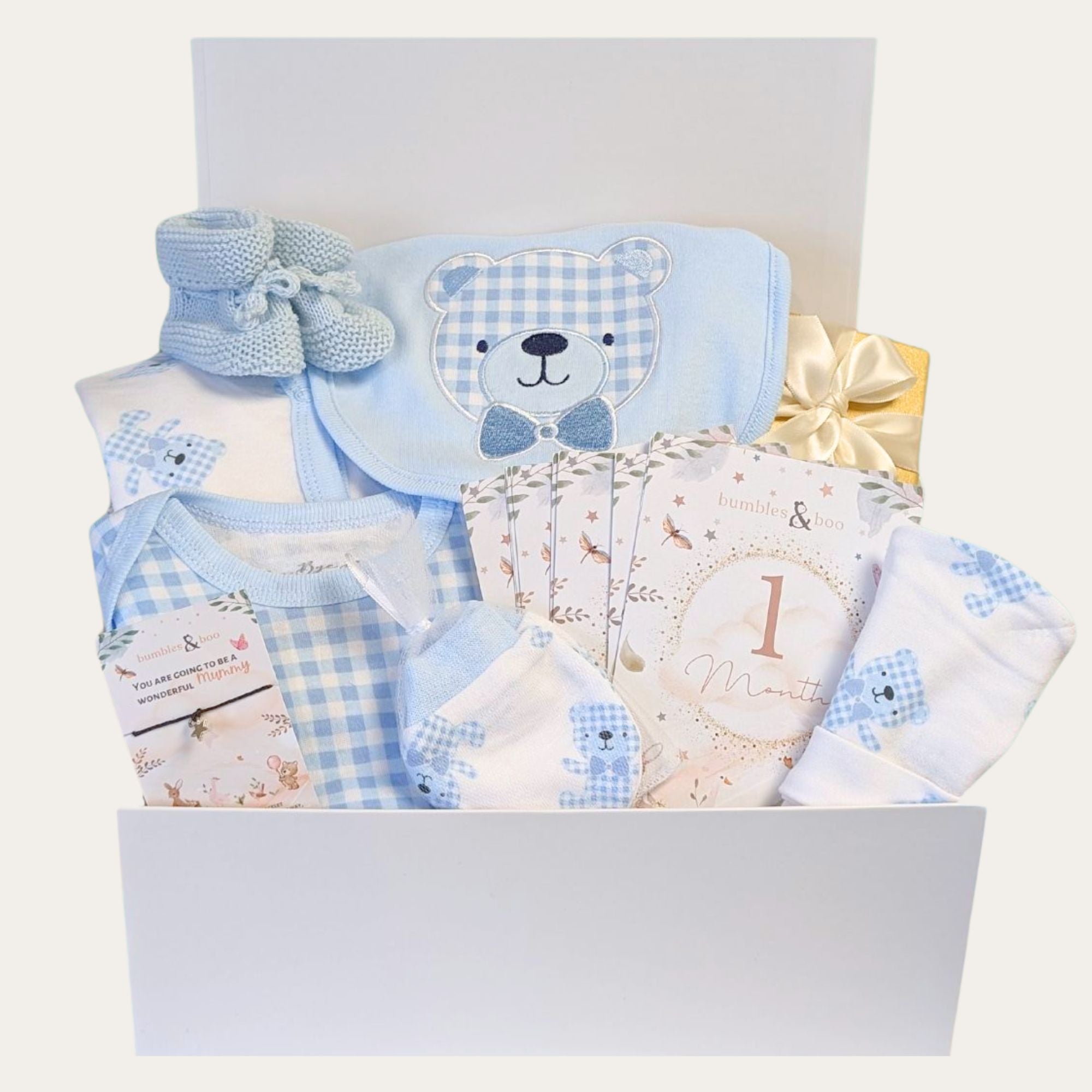 Baby shower gifts for boys packed in a white gift box. Hamper contains blue baby boy clothes with blue bear design among other presents.