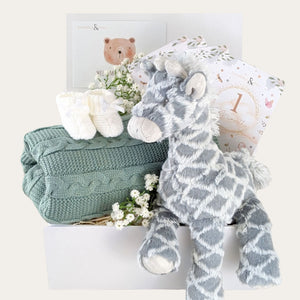 Baby shower gifts hamper box with large grey giraffe, green knit blanket, baby knit booties and milestone cards.