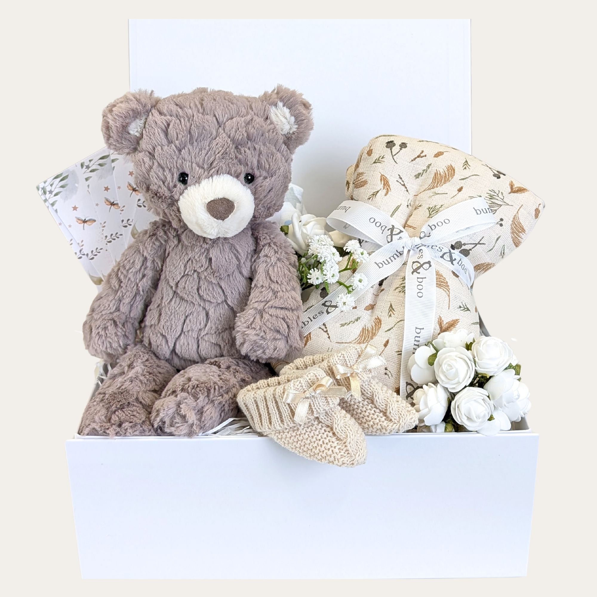 Baby shower hamper gifts box with newborn presents including teddy bear, large muslin swaddle, baby booties and milestone cards. 