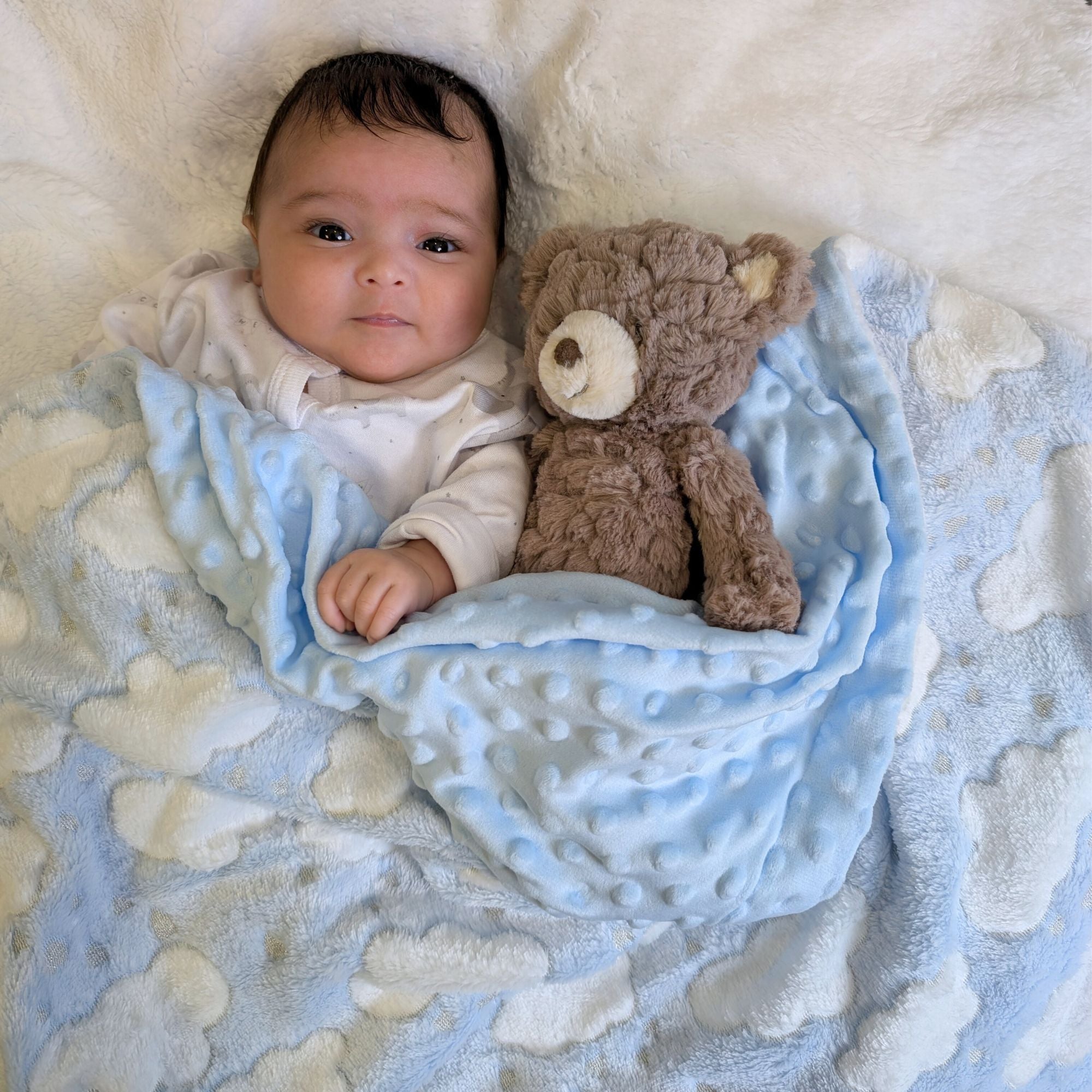 A soft blue baby blanket wrap with a white cloud pattern on the front and blue dimple backing on the back bumbles and boo