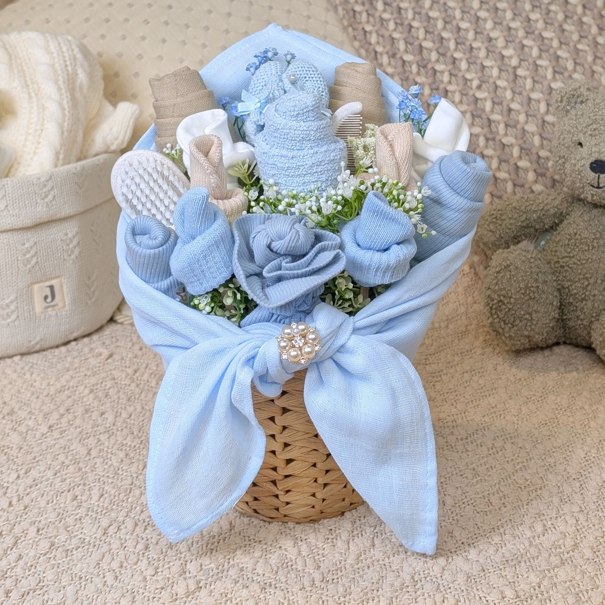 stunning blue and beige baby clothing flower bouquet presented in a rattan plant pot. contains mittens, muslins, hats, bibs, booties. Bumbles and boo. 