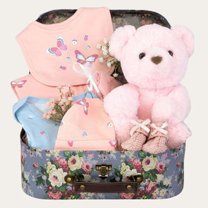 Baby girl gifts in a vintage hamper keepsake box. Presents include clothes set and pink teddy.