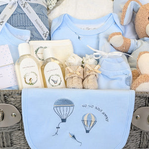 close up of a baby boy gifts hamper with blue clothing set with hot air balloons on it, baby booties and organic baby wash