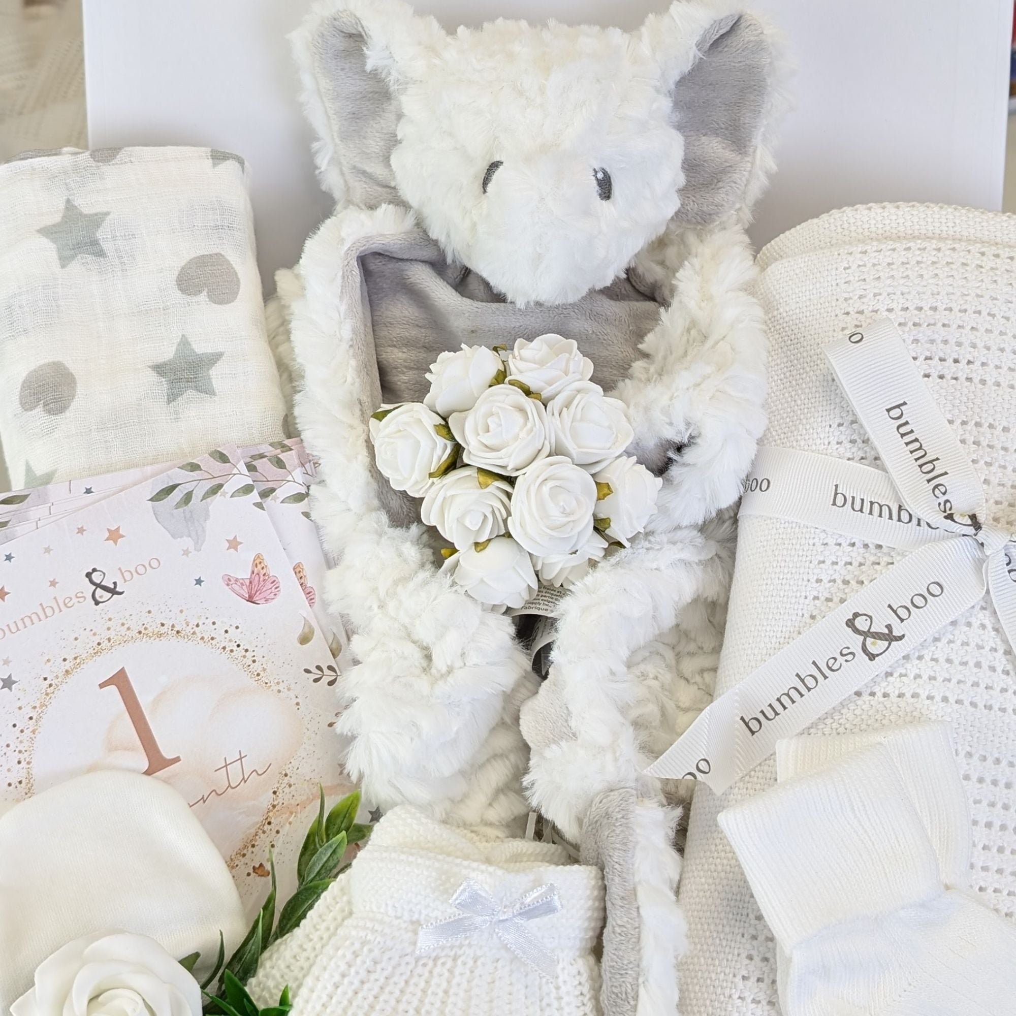 close up of a new baby gifts box with elephant comforter, white baby blanket, cards, muslin and baby sock and mittens