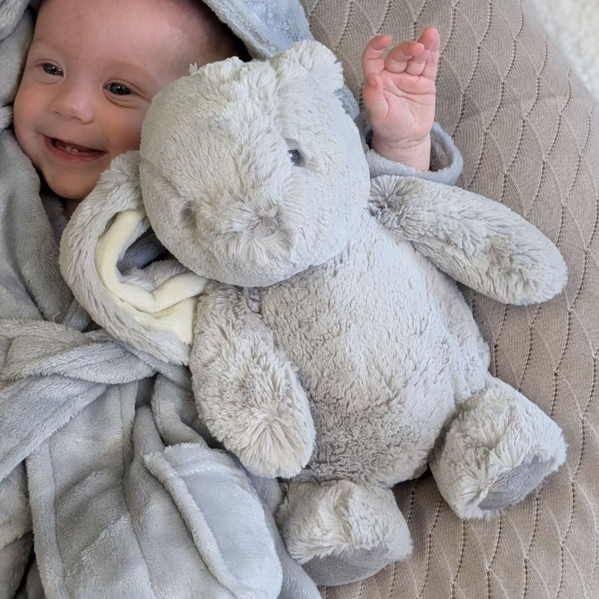 Baby with large grey rabbit soft toy.