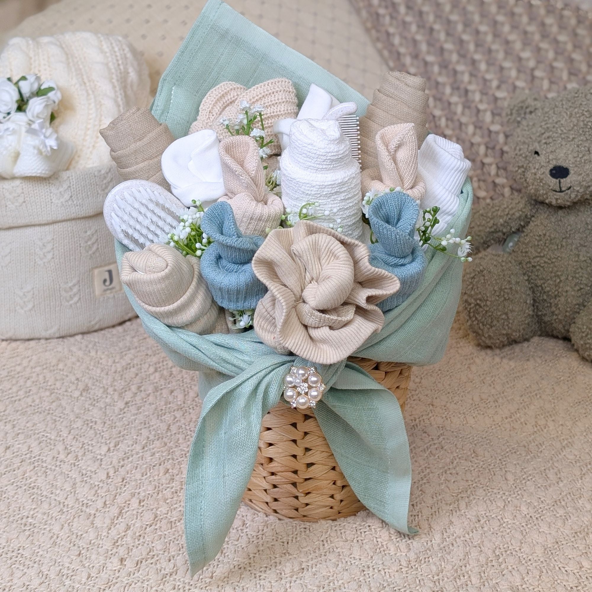 stunning sage green and beige baby clothing flower bouquet presented in a rattan plant pot. contains mittens, muslins, hats, bibs, booties. Bumbles and boo. 