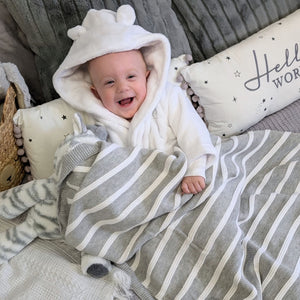 Happy baby covered in a grey and white baby striped blanket.