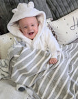 Happy baby covered in a grey and white baby striped blanket.