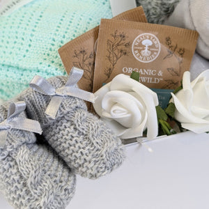 Close up of baby booties, organic tea and decorative flower.