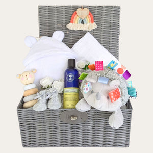 Baby gifts in a hamper basket. Includes dressing gown, cellular blanket, hedgehog, baby lotion, baby booties and wooden toy.