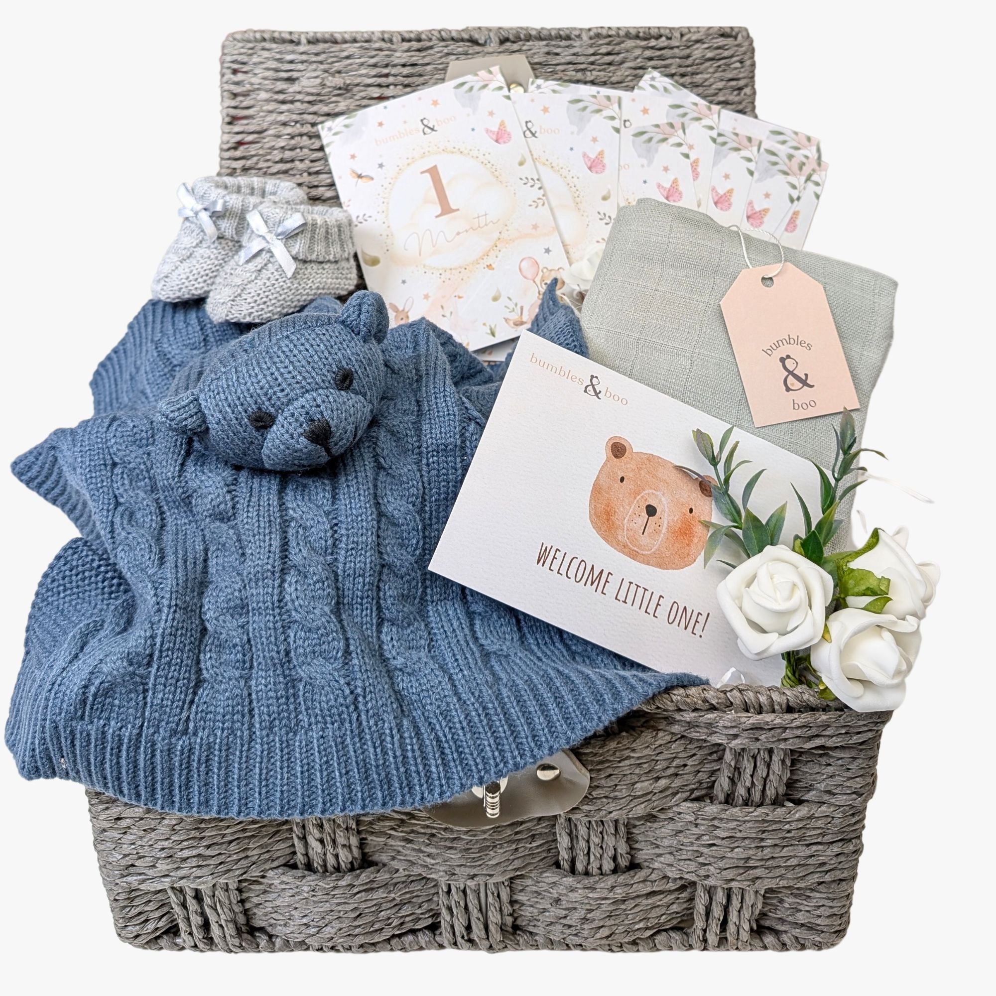 A beautifully curated baby gift basket in dusky blue tones, featuring a knit bear comforter, recycled muslin square, cosy knit booties, eco-friendly milestone cards, and a greetings card—perfect for celebrating a baby boy's arrival. Bumbles and Boo