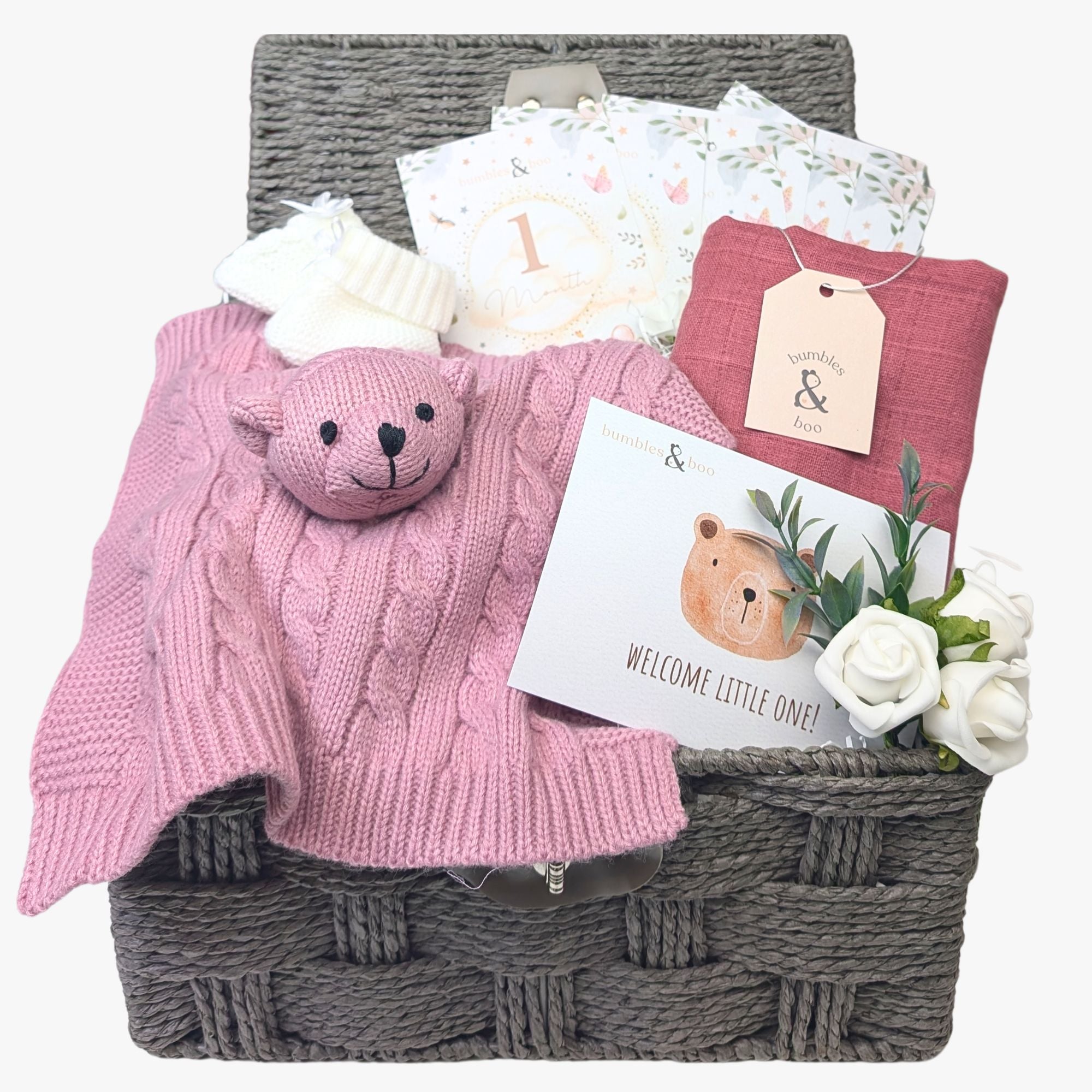 A beautifully curated baby gift basket in dusky pink tones, featuring a knit bear comforter, recycled muslin square, cosy knit booties, eco-friendly milestone cards, and a greetings card—perfect for celebrating a new arrival. Bumbles and Boo.