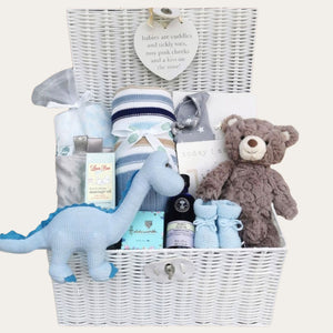 Large new baby boy gifts hamper with blue dinosaur, stripy blanket and teddy bear in a white hamper basket.