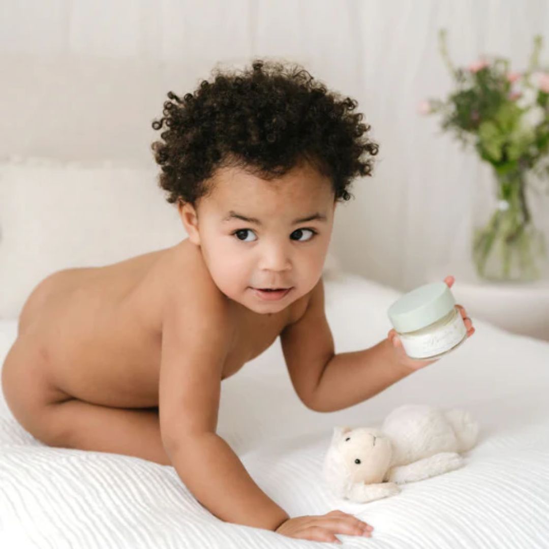 Cute baby holding a pot of little butterfly baby nappy cream.