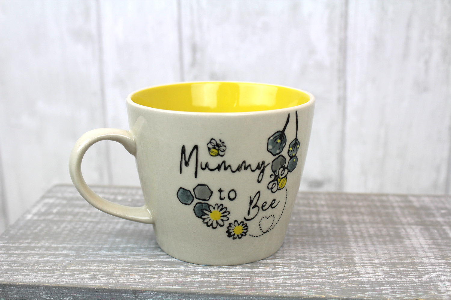 A ceramic mug with 'Mummy To Bee' writing on the front with a picture of a bumble bee and honeycomb with a yellow inside