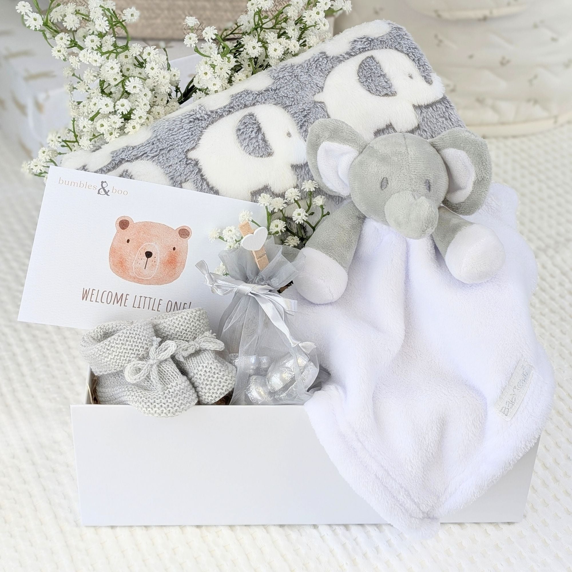 new baby gifts basket with an elephant blanket and elephant soft toy. Chocolates for mum and baby booties in grey.