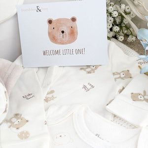 Greetings card with welcome little one on it and close up of baby clothing set.