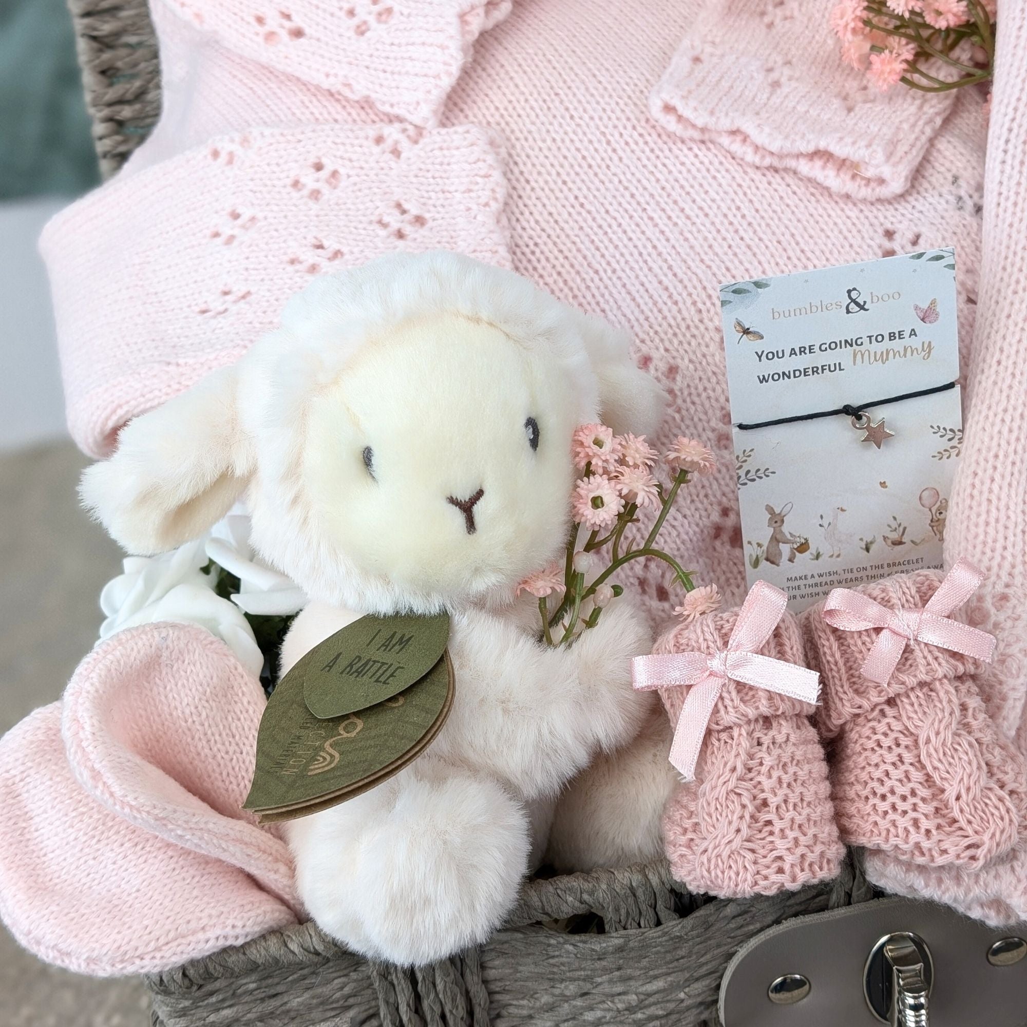 new baby girl gifts basket with pink knit clothing, lamb soft toy, baby booties and a bracelet for mum.