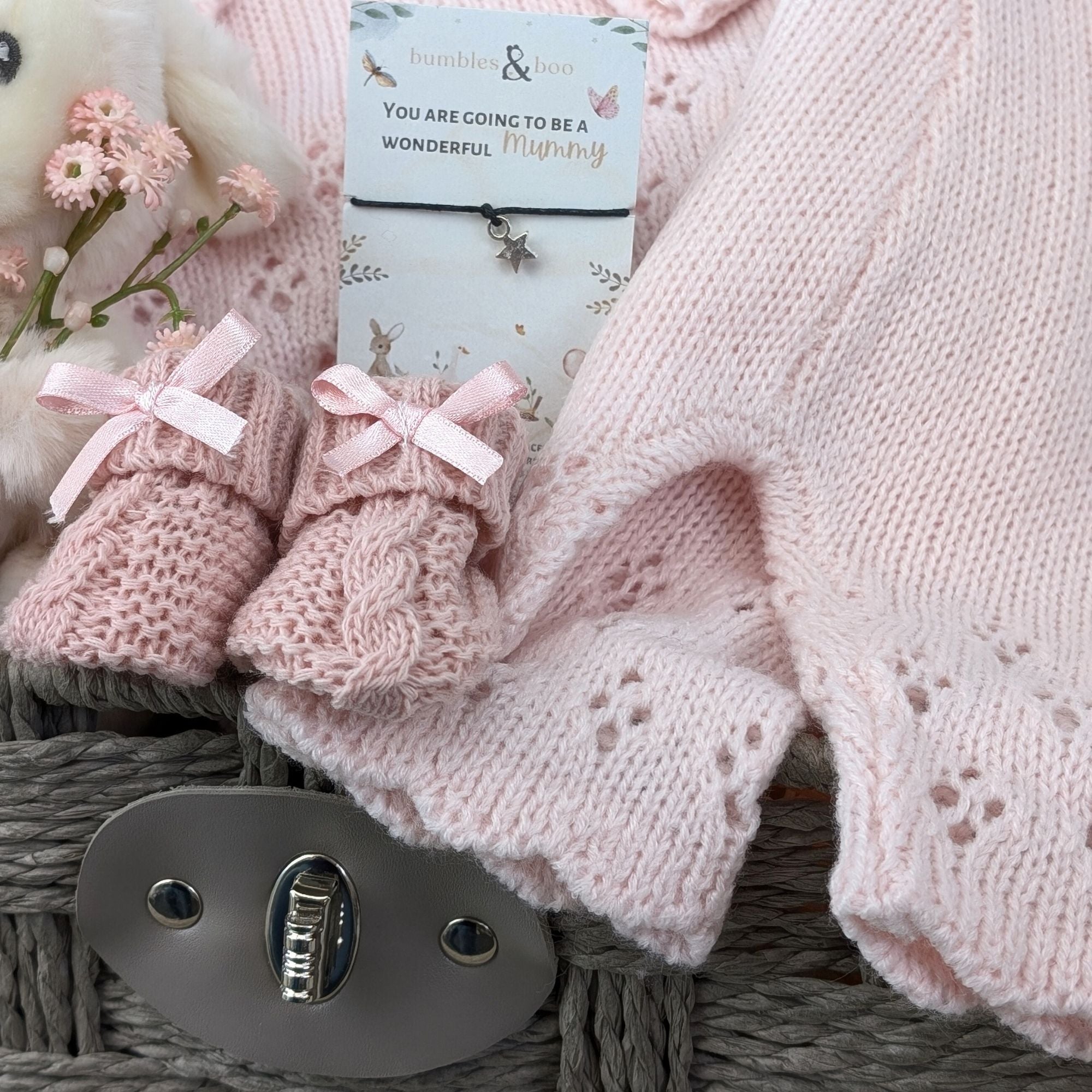 new baby girl gifts basket with pink knit clothing, lamb soft toy, baby booties and a bracelet for mum.