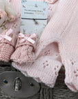 new baby girl gifts basket with pink knit clothing, lamb soft toy, baby booties and a bracelet for mum.