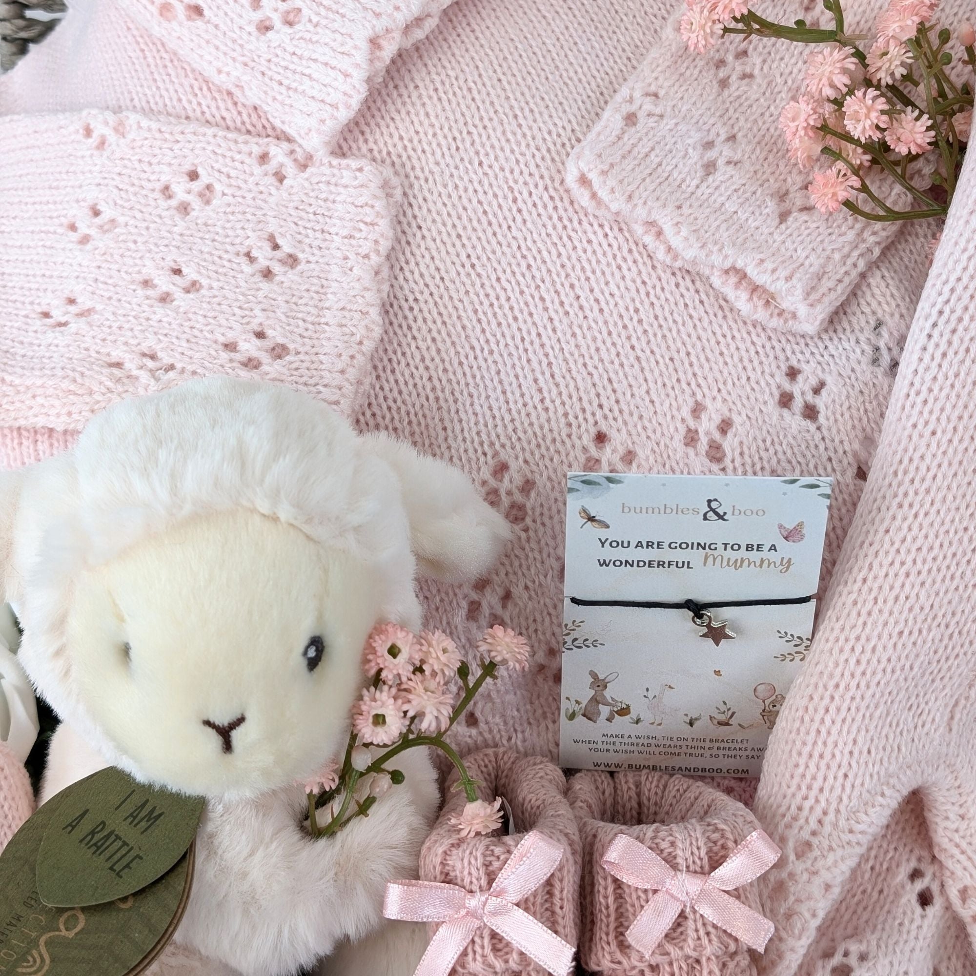 new baby girl gifts basket with pink knit clothing, lamb soft toy, baby booties and a bracelet for mum.