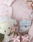 new baby girl gifts basket with pink knit clothing, lamb soft toy, baby booties and a bracelet for mum.