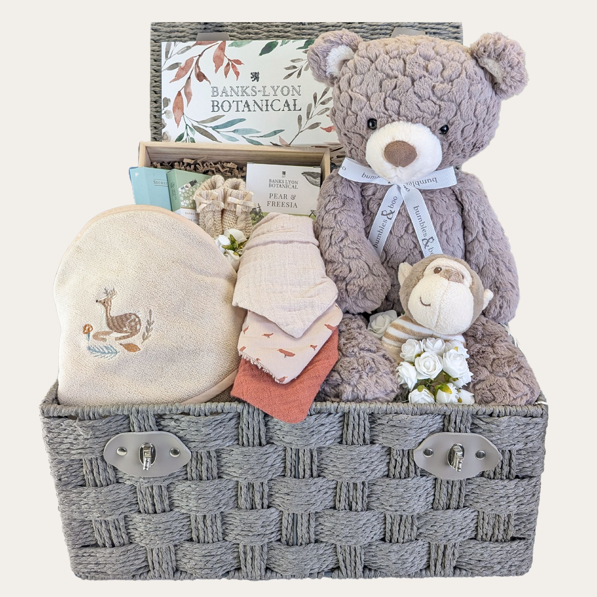 Baby gifts in a hamper basket with brown teddy bear and baby towel.