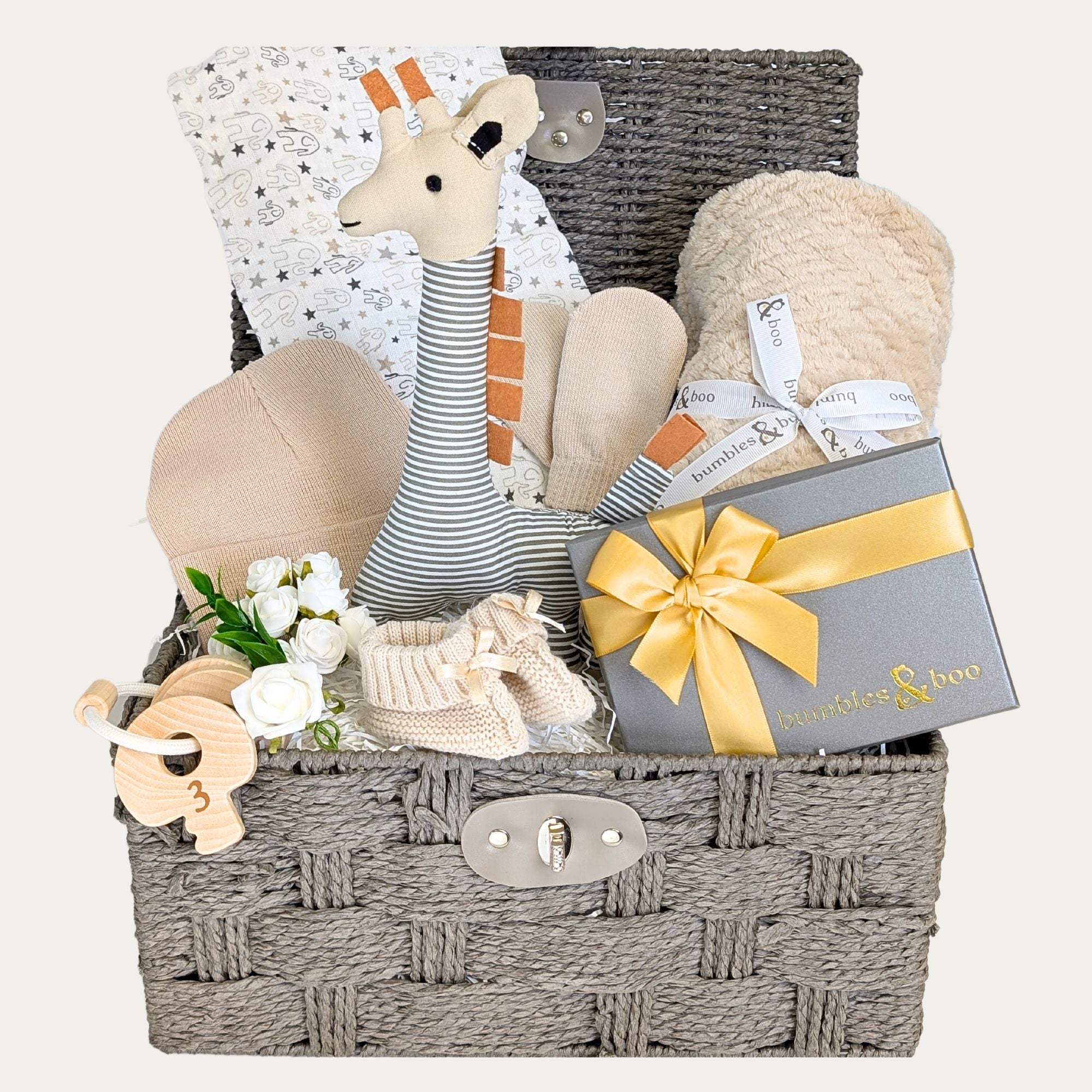 baby gift hamper with a cuddly giraffe soft toy, biscuit-toned blanket, knit hat, booties, mittens, 100% cotton muslin square, and sensory teething toy keys. Bumbles and Boo