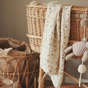 Organic baby muslin swaddle blanket grasslands pattern hanging from a moses basket.