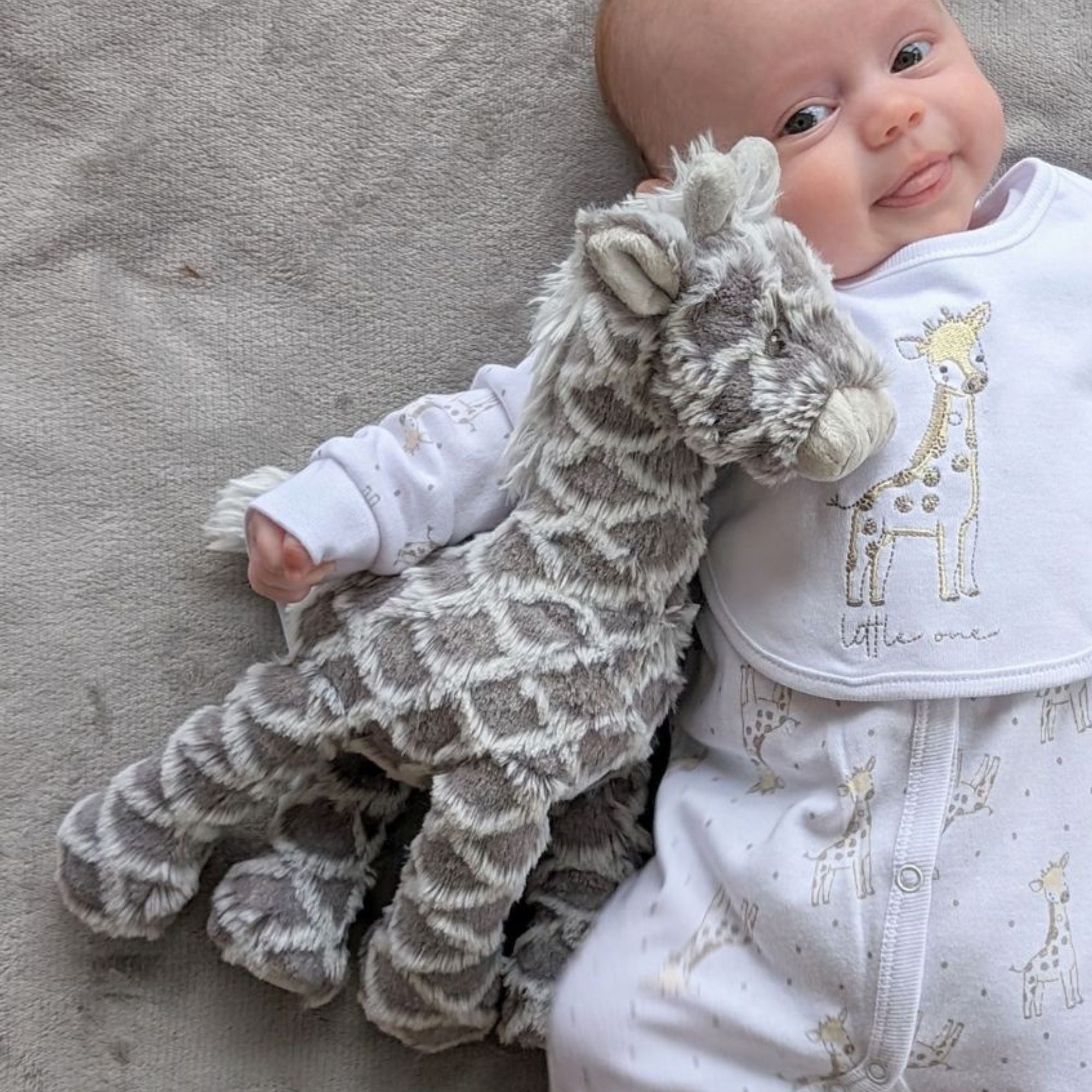 Grey giraffe mary meyer baby toy, with a smiling baby.